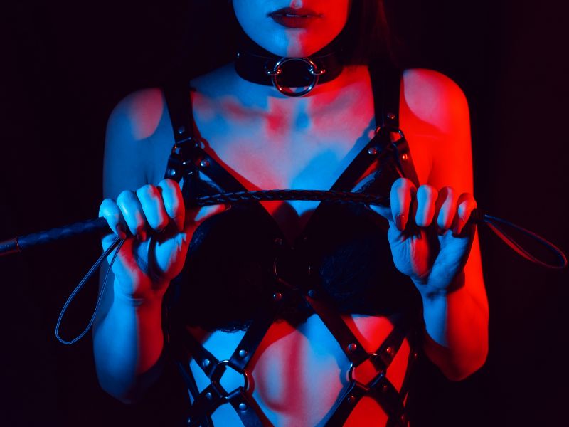 dominatrice avec un collier BDSM et un fouet entre les mains