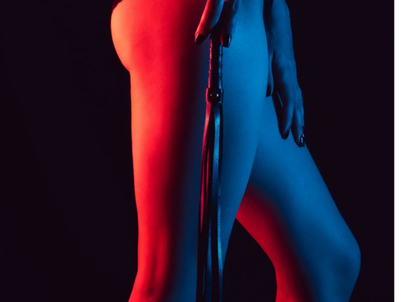 Dominatrice qui tient un martinet le long de ses cuisses