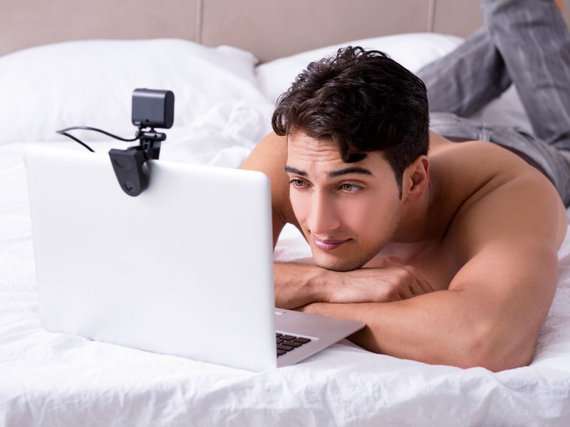 homme qui fait une webcam, allongé sur le ventre dans son lit